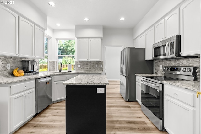 kitchen with appliances with stainless steel finishes, light wood-type flooring, light stone counters, sink, and a center island