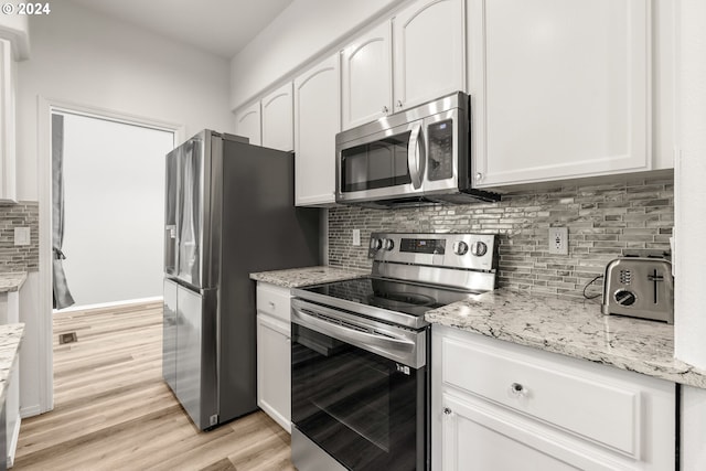 kitchen with light stone countertops, light hardwood / wood-style flooring, white cabinets, and stainless steel appliances