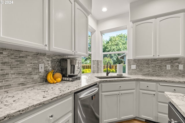 kitchen with white cabinetry, sink, light stone countertops, stainless steel dishwasher, and backsplash