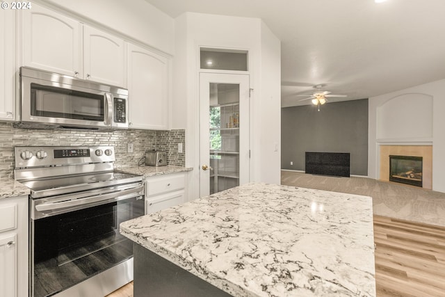 kitchen with ceiling fan, light wood-type flooring, appliances with stainless steel finishes, white cabinetry, and a tiled fireplace