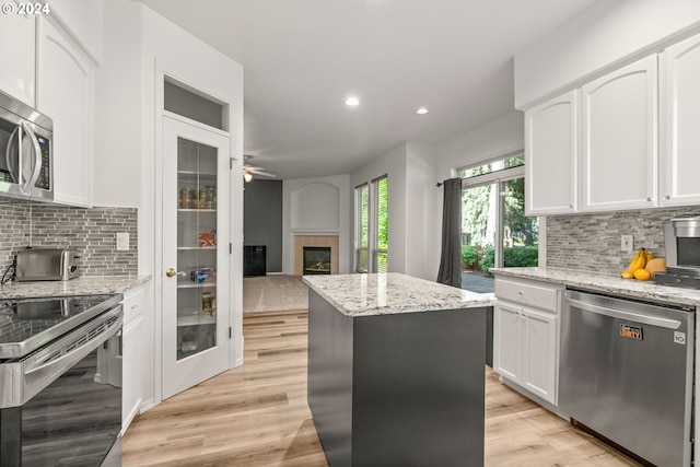 kitchen with white cabinetry, a center island, light stone countertops, and appliances with stainless steel finishes