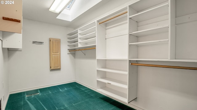 spacious closet with a skylight and dark colored carpet