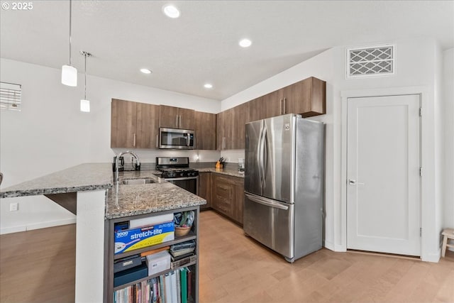 kitchen featuring appliances with stainless steel finishes, a sink, a peninsula, light stone countertops, and decorative light fixtures