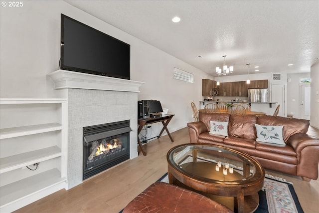 living area featuring a chandelier, a tiled fireplace, recessed lighting, a textured ceiling, and wood finished floors