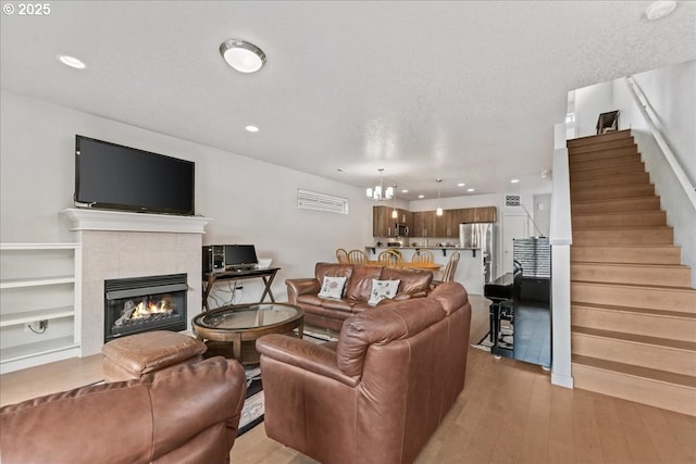 living area featuring a tiled fireplace, light wood-style flooring, stairs, a chandelier, and recessed lighting