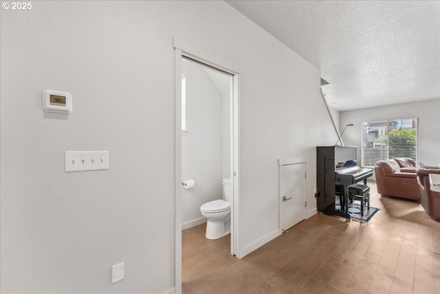 hall featuring wood finished floors, a textured ceiling, and baseboards