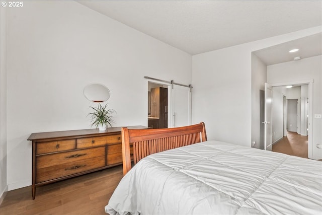 bedroom featuring wood finished floors, a barn door, and baseboards