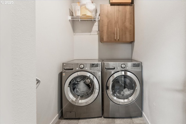 clothes washing area with cabinet space, washer and dryer, and baseboards