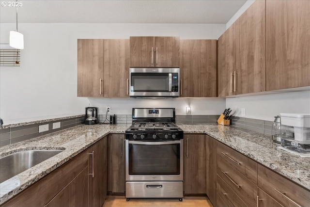 kitchen with appliances with stainless steel finishes, a sink, light stone countertops, decorative light fixtures, and modern cabinets
