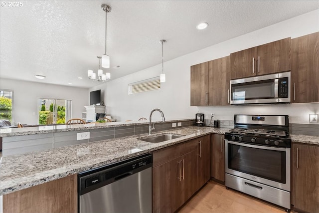 kitchen featuring stainless steel appliances, a sink, light stone counters, pendant lighting, and a textured ceiling