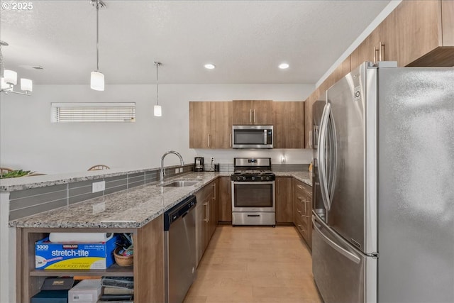 kitchen with stainless steel appliances, a sink, brown cabinetry, light stone countertops, and recessed lighting