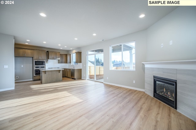 unfurnished living room featuring baseboards, a tile fireplace, light wood-style flooring, a sink, and recessed lighting