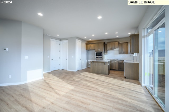 kitchen with a kitchen island, brown cabinets, open floor plan, stainless steel appliances, and light countertops