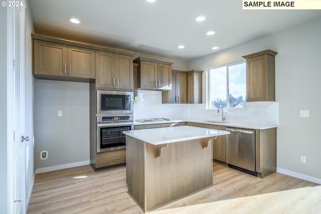 kitchen featuring stainless steel appliances, light countertops, light wood-style flooring, a sink, and a kitchen island