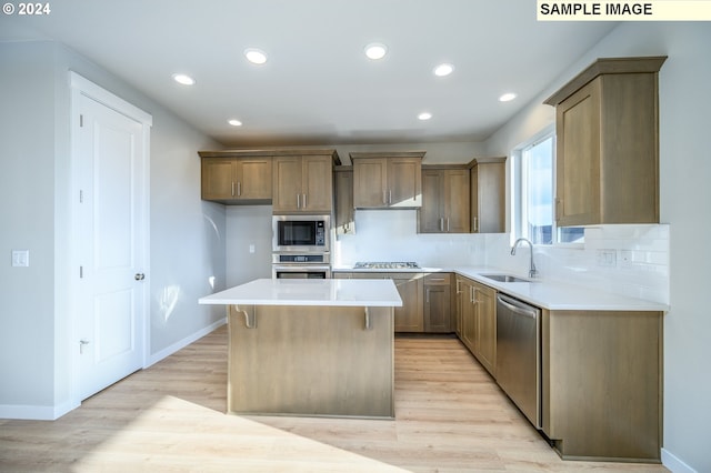 kitchen with light countertops, appliances with stainless steel finishes, brown cabinetry, a kitchen island, and a sink