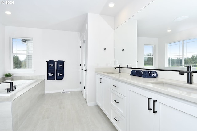 bathroom featuring tile floors, dual bowl vanity, tiled tub, and a wealth of natural light