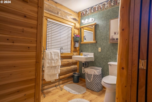 bathroom with toilet, sink, log walls, and hardwood / wood-style flooring