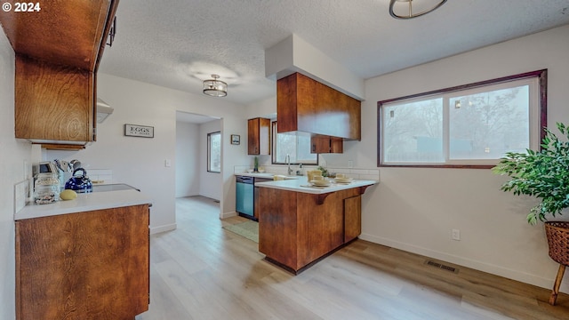 kitchen with light wood-type flooring, kitchen peninsula, sink, stainless steel dishwasher, and a textured ceiling