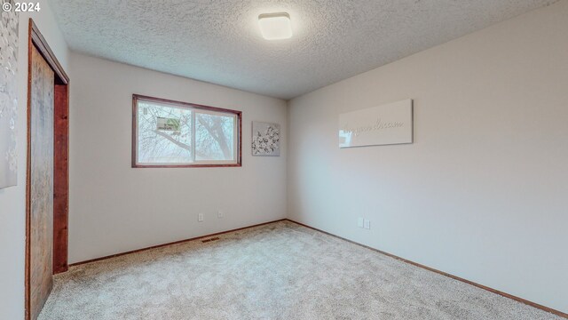 unfurnished bedroom with a textured ceiling, light carpet, and a closet