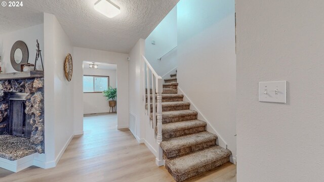 staircase featuring wood-type flooring, a stone fireplace, and a textured ceiling