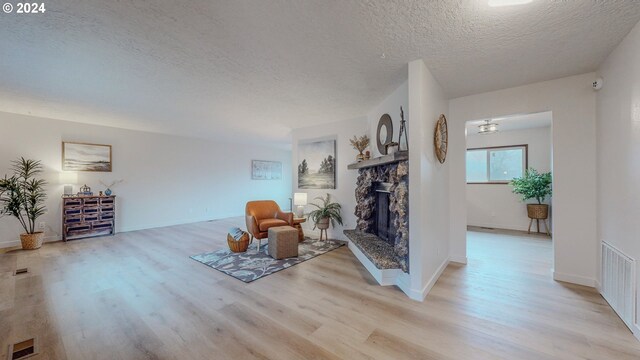 unfurnished room featuring light wood-type flooring, a textured ceiling, and a stone fireplace