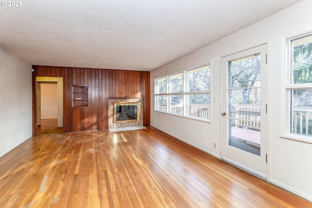 unfurnished living room with a brick fireplace, hardwood / wood-style flooring, wood walls, and a textured ceiling