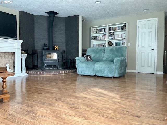 living room with a wood stove, a textured ceiling, baseboards, and wood finished floors