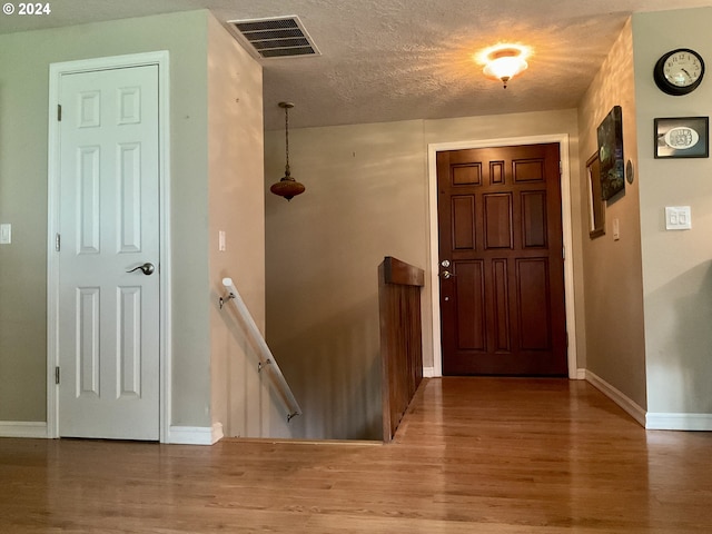 foyer entrance featuring a textured ceiling, wood finished floors, visible vents, and baseboards