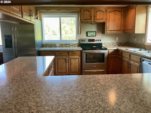 kitchen featuring appliances with stainless steel finishes, brown cabinets, a sink, and tasteful backsplash