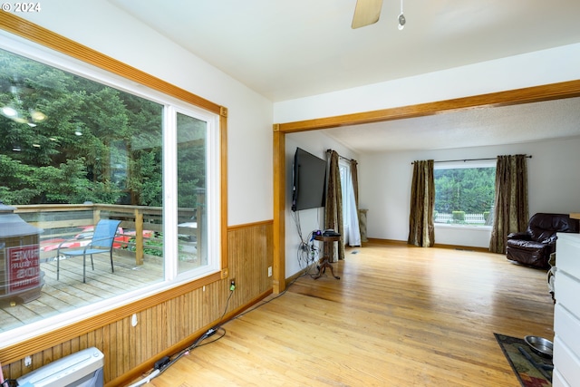 living room with ceiling fan, light wood-type flooring, and wooden walls