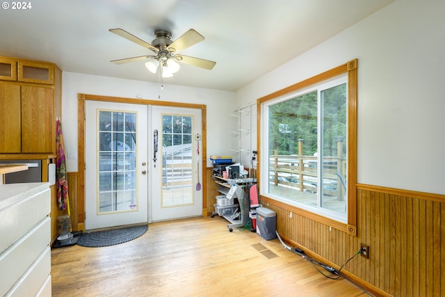 doorway with ceiling fan, french doors, wooden walls, and light hardwood / wood-style flooring