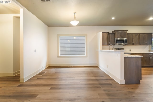 kitchen with wood-type flooring, appliances with stainless steel finishes, hanging light fixtures, dark brown cabinetry, and sink