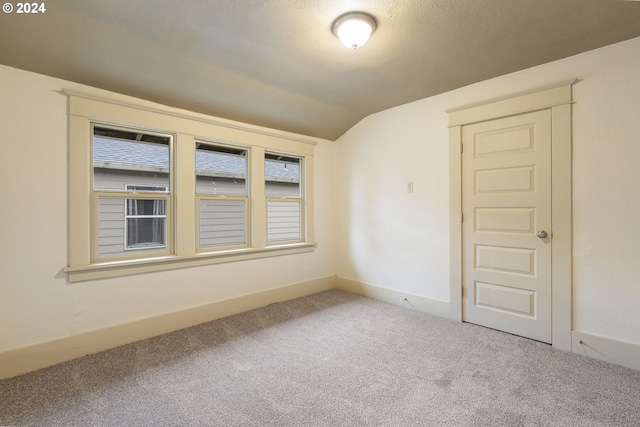 unfurnished room featuring a textured ceiling, vaulted ceiling, and carpet floors