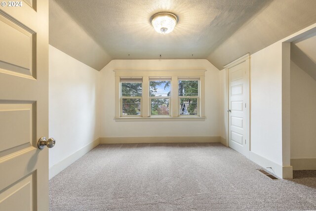 bonus room featuring lofted ceiling, light colored carpet, and a textured ceiling