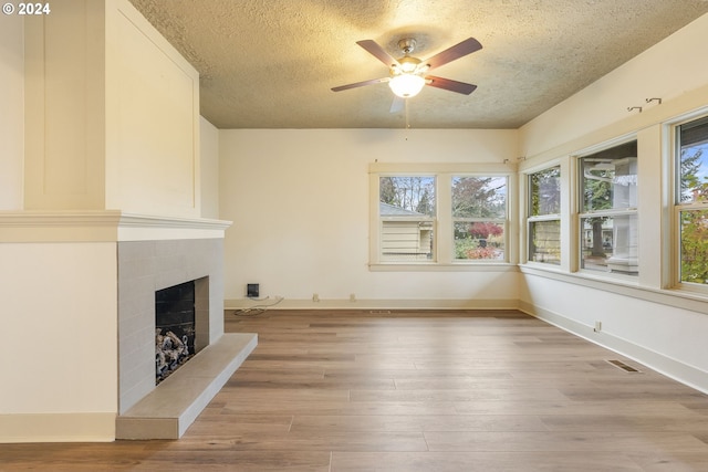 unfurnished living room featuring a tile fireplace, a textured ceiling, ceiling fan, and light wood-type flooring