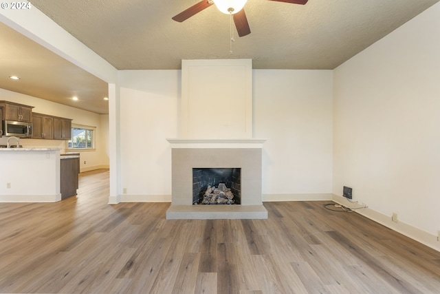 unfurnished living room featuring a fireplace, a textured ceiling, ceiling fan, and light hardwood / wood-style floors