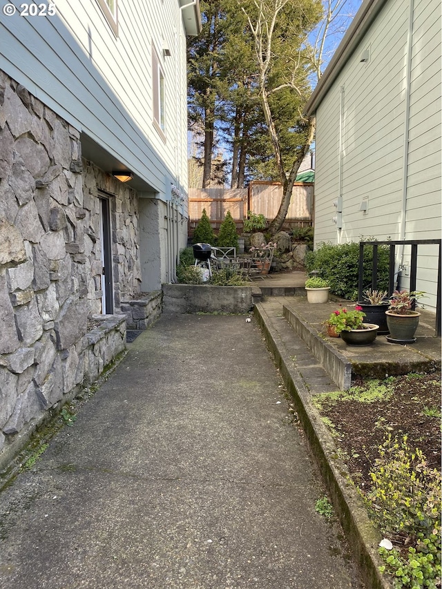 view of side of home featuring stone siding, a patio, and fence