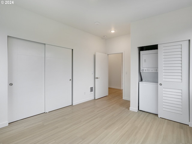 unfurnished bedroom featuring a closet, light hardwood / wood-style floors, and stacked washer / dryer