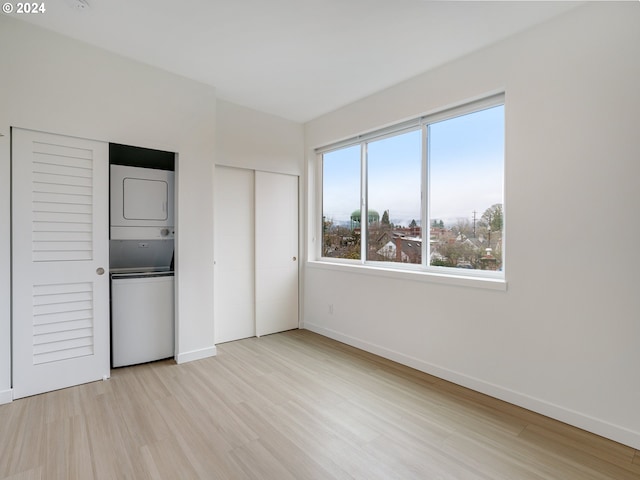 unfurnished bedroom with light hardwood / wood-style floors and stacked washing maching and dryer