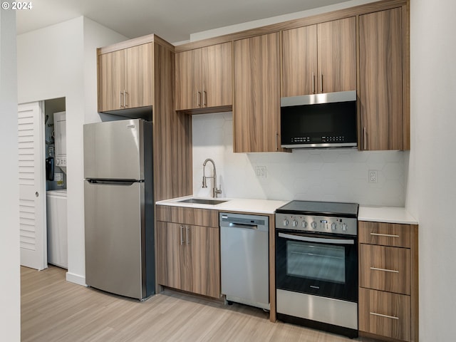 kitchen with sink, light hardwood / wood-style flooring, backsplash, stacked washer and dryer, and appliances with stainless steel finishes