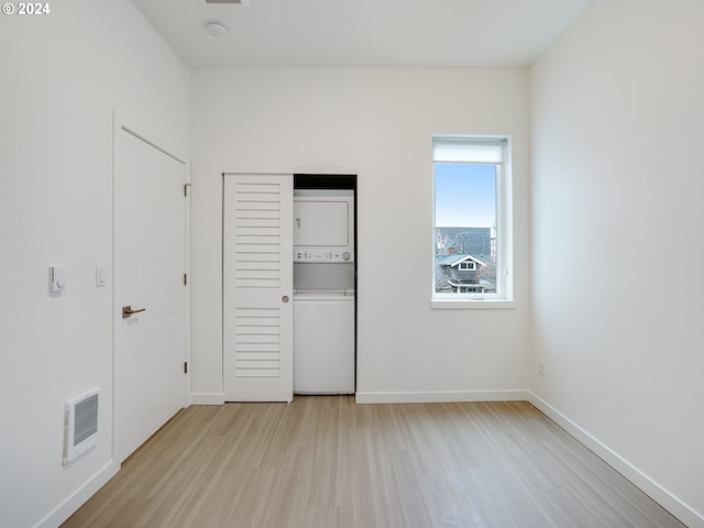 unfurnished bedroom with stacked washing maching and dryer, heating unit, and light wood-type flooring