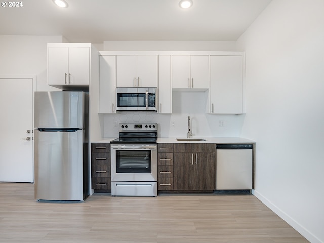 kitchen featuring decorative backsplash, light wood-type flooring, white cabinets, appliances with stainless steel finishes, and sink