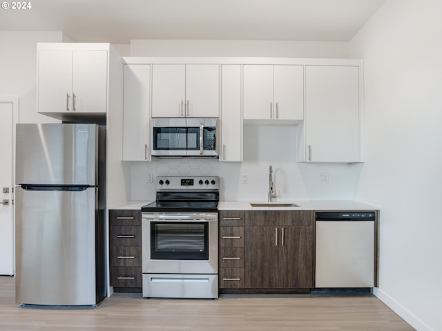 kitchen featuring sink, light hardwood / wood-style floors, white cabinetry, appliances with stainless steel finishes, and dark brown cabinetry