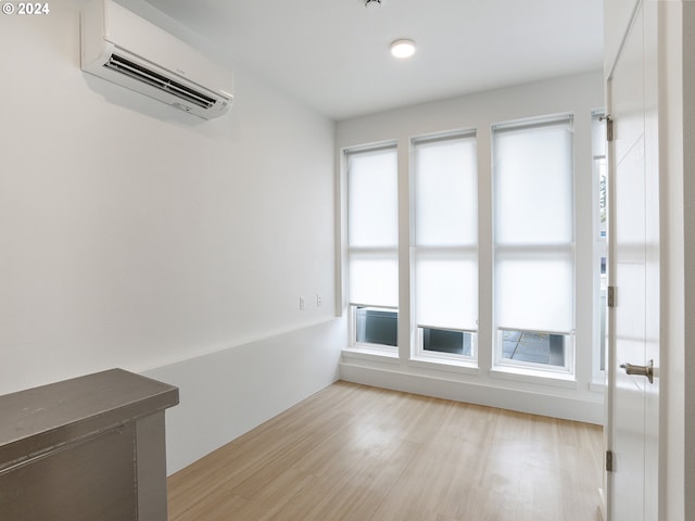 spare room with an AC wall unit, a wealth of natural light, and light hardwood / wood-style flooring