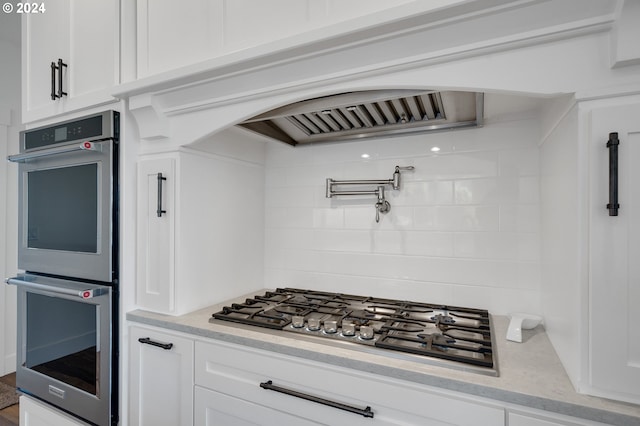 kitchen with stainless steel appliances, white cabinetry, and light stone counters