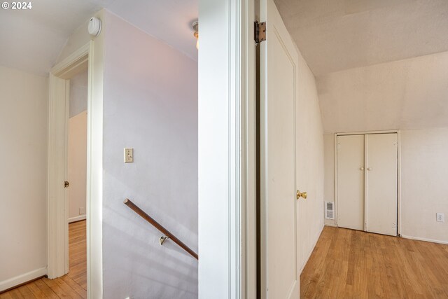 corridor with light wood-type flooring and vaulted ceiling