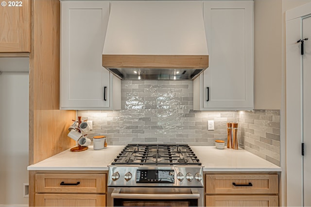 kitchen featuring white cabinets, premium range hood, backsplash, and high end range