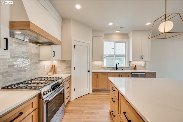 kitchen with premium range hood, hanging light fixtures, sink, white cabinetry, and stainless steel appliances