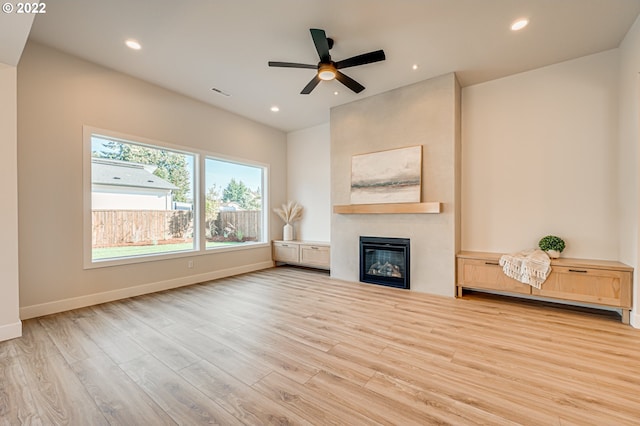 unfurnished living room featuring a large fireplace, light hardwood / wood-style floors, and ceiling fan