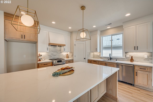 kitchen with sink, white cabinets, light hardwood / wood-style flooring, stainless steel appliances, and premium range hood